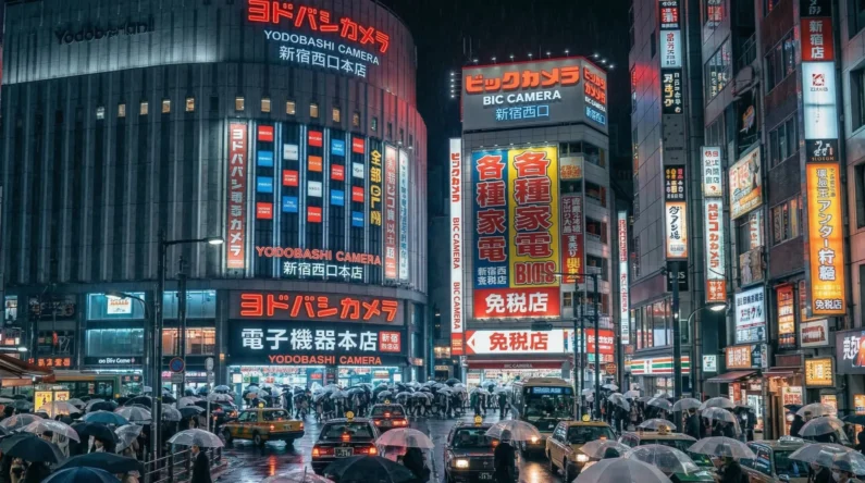 Guía de bic camera y yodobashi: ¿dónde es mejor comprar tecnología en japón? - bic camera vs yodobashi guia compras 2026 japon Fachadas gigantes iluminadas con luces de neón de las tiendas de electrónica bic camera y yodobashi camera en tokio bajo la lluvia.