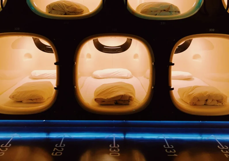 Dormir en hoteles cápsula: el método auténtico para ahorrar en japón - hotel capsula tokio clasico clase economica Matriz frontal de cápsulas de dormir económicas en tokio con iluminación cálida y numeración de neón en el suelo. Una de las mejores formas de experimentar los hoteles cápsula en japón