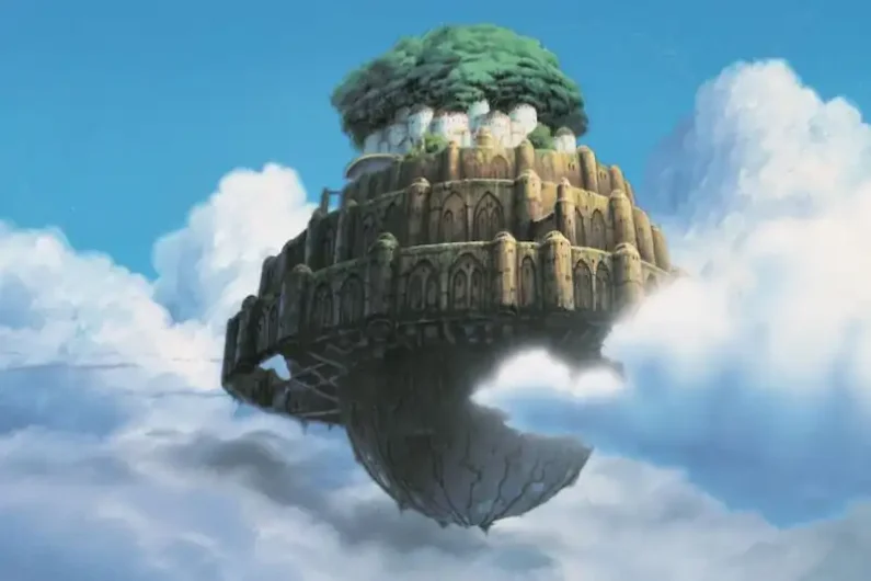 Ranking studio ghibli: las mejores películas de miyazaki - el castillo en el cielo y los primeros pasos de ghibli Fotograma de animación que muestra una inmensa ciudad antigua y cubierta de vegetación flotando en medio de un cielo azul con nubes blancas.