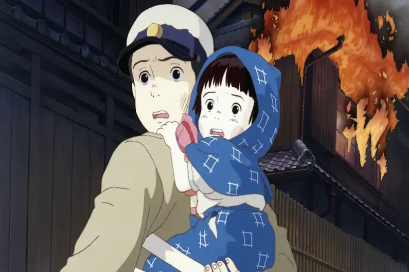 Ranking studio ghibli: las mejores películas de miyazaki - la tumba de las luciernagas y la dura realidad de ghibli Fotograma de animación que muestra a un joven japonés con expresión de miedo llevando en brazos a su hermana pequeña cubierta con una manta azul mientras un edificio arde al fondo.