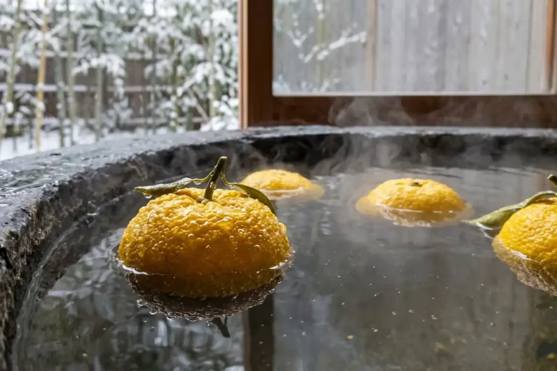El baño japonés (ofuro): descubre el secreto del relax absoluto - bano yuzu solsticio invierno japon Frutas amarillas de yuzu flotando en el agua humeante de una bañera de piedra oscura.