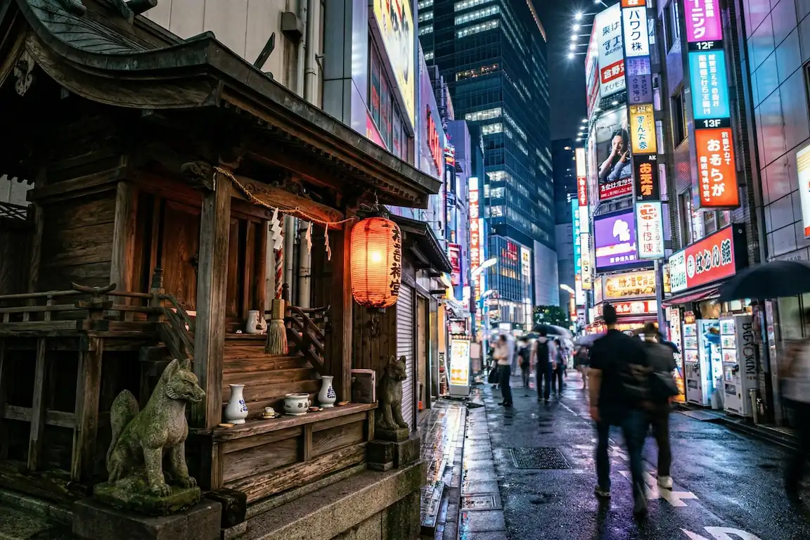 Supersticiones japonesas y tabúes: números, palillos y espejos - contrastes japon tecnologia supersticiones Pequeño santuario sintoísta tradicional de madera oscura situado en una calle de shinjuku, iluminado por los reflejos de carteles de neón modernos sobre asfalto mojado.