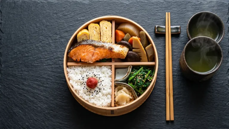 Cultura del bento: el arte de la caja de comida para llevar en japón - guia bento japones cultura gastronomia Una caja bento de cedro perfectamente organizada con arroz, pescado y vegetales sobre una mesa oscura.