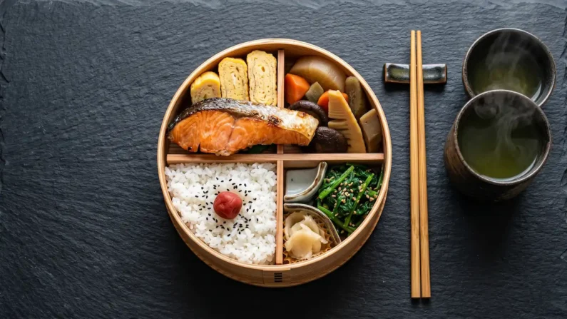 Cultura del bento: el arte de la caja de comida para llevar en japón - guia bento japones cultura gastronomia Una caja bento de cedro perfectamente organizada con arroz, pescado y vegetales sobre una mesa oscura.