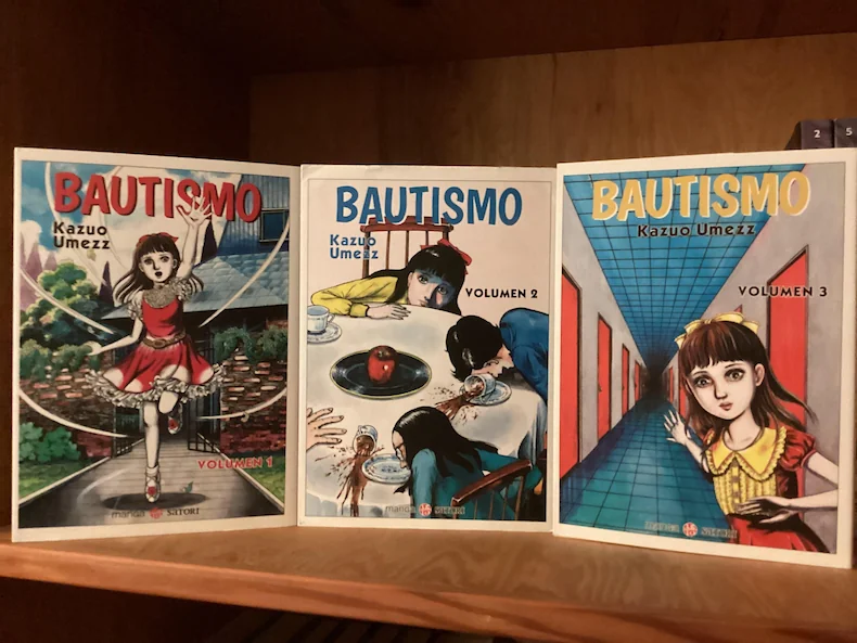 5 autores de manga de terror más perturbadores que junji ito - kazuo umezu bautismo manga fisico Tres tomos físicos del manga bautismo de kazuo umezu alineados de frente sobre una estantería de madera clásica.