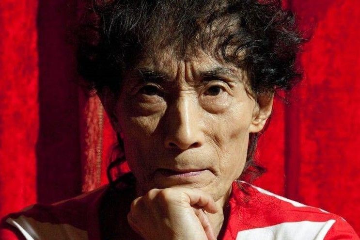 5 autores de manga de terror más perturbadores que junji ito - kazuo umezu mangaka retrato creador Retrato fotográfico de kazuo umezu, un hombre japonés mayor vistiendo una icónica camiseta de rayas horizontales rojas y blancas.