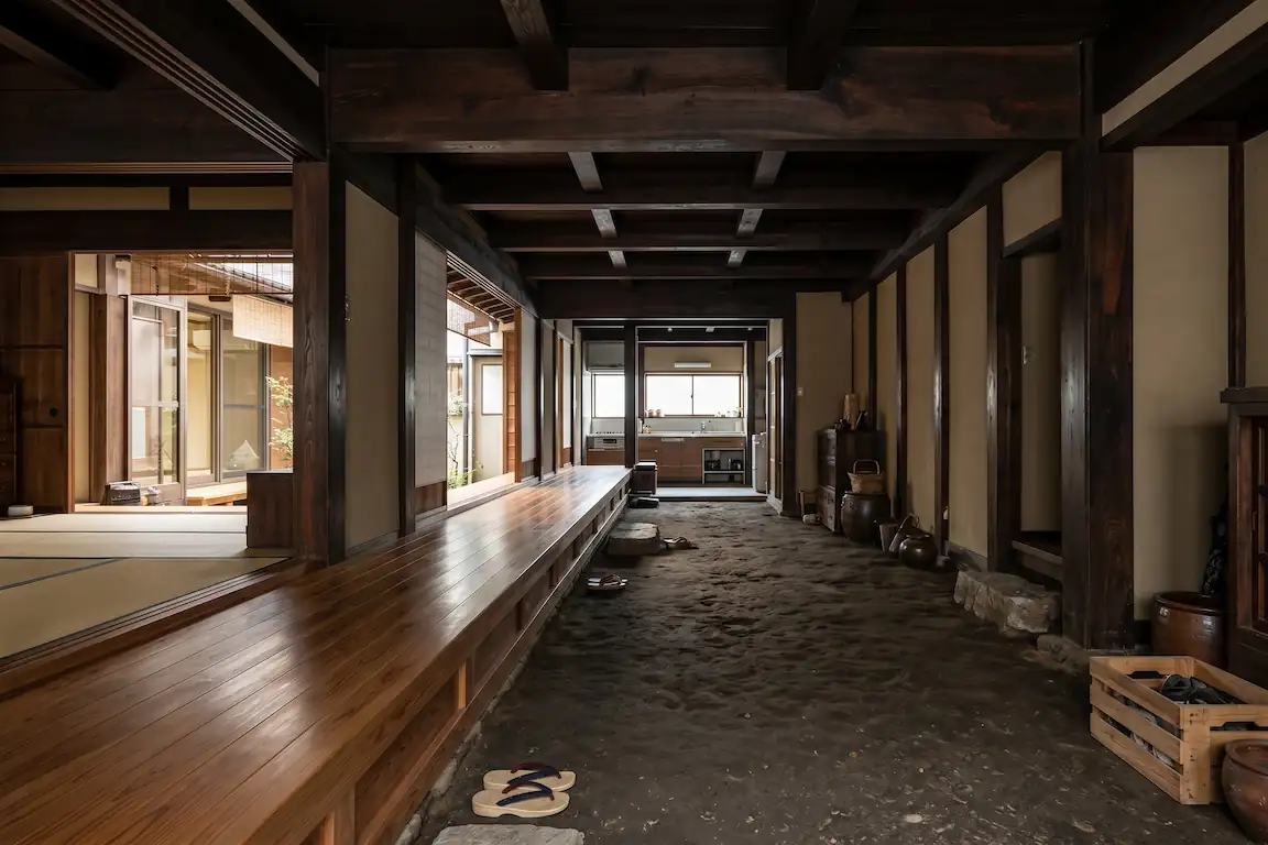Dormir en una machiya: la experiencia más auténtica de japón - pasillo doma machiya kioto Pasillo largo con suelo de tierra y vigas de madera vista en una casa tradicional japonesa.
