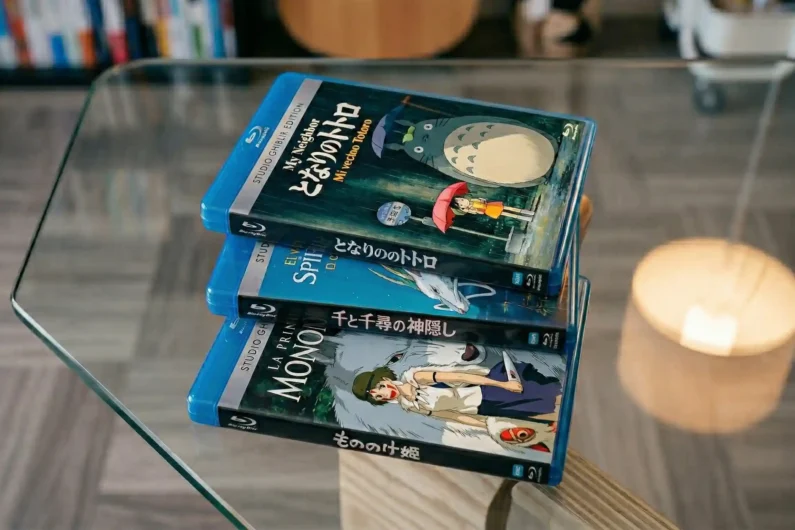 Ranking studio ghibli: las mejores películas de miyazaki - ranking mejores peliculas studio ghibli miyazaki Fotografía de una pila de bluray japonesas de studio ghibli iluminadas por una lámpara cálida