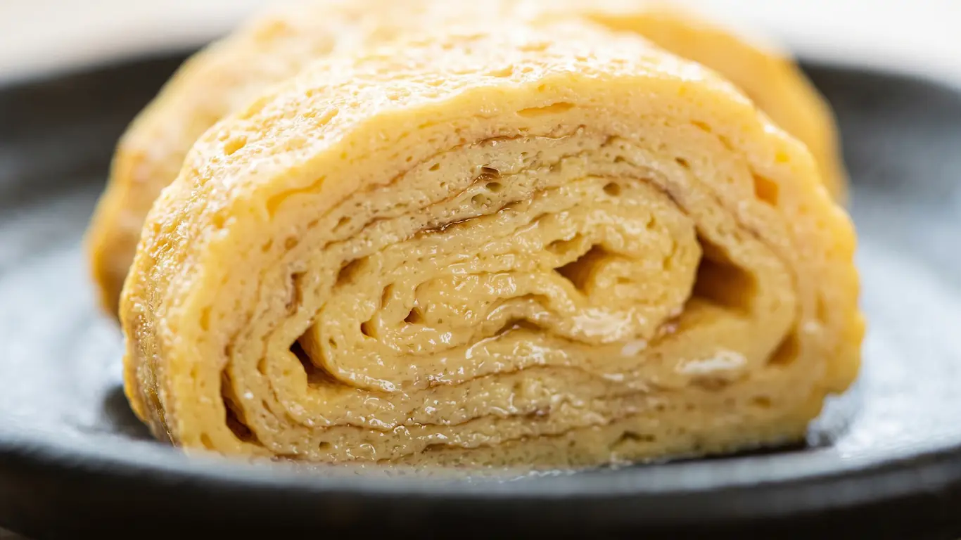 Desayuno japonés, diferencias entre el estilo tradicional y el occidental - tamagoyaki tortilla japonesa dashi Plano detalle macro de las capas finas y jugosas de una tortilla enrollada tamagoyaki con humedad de caldo dashi. El tamagoyaki es parte inconfundible del desayuno tradicional japonés
